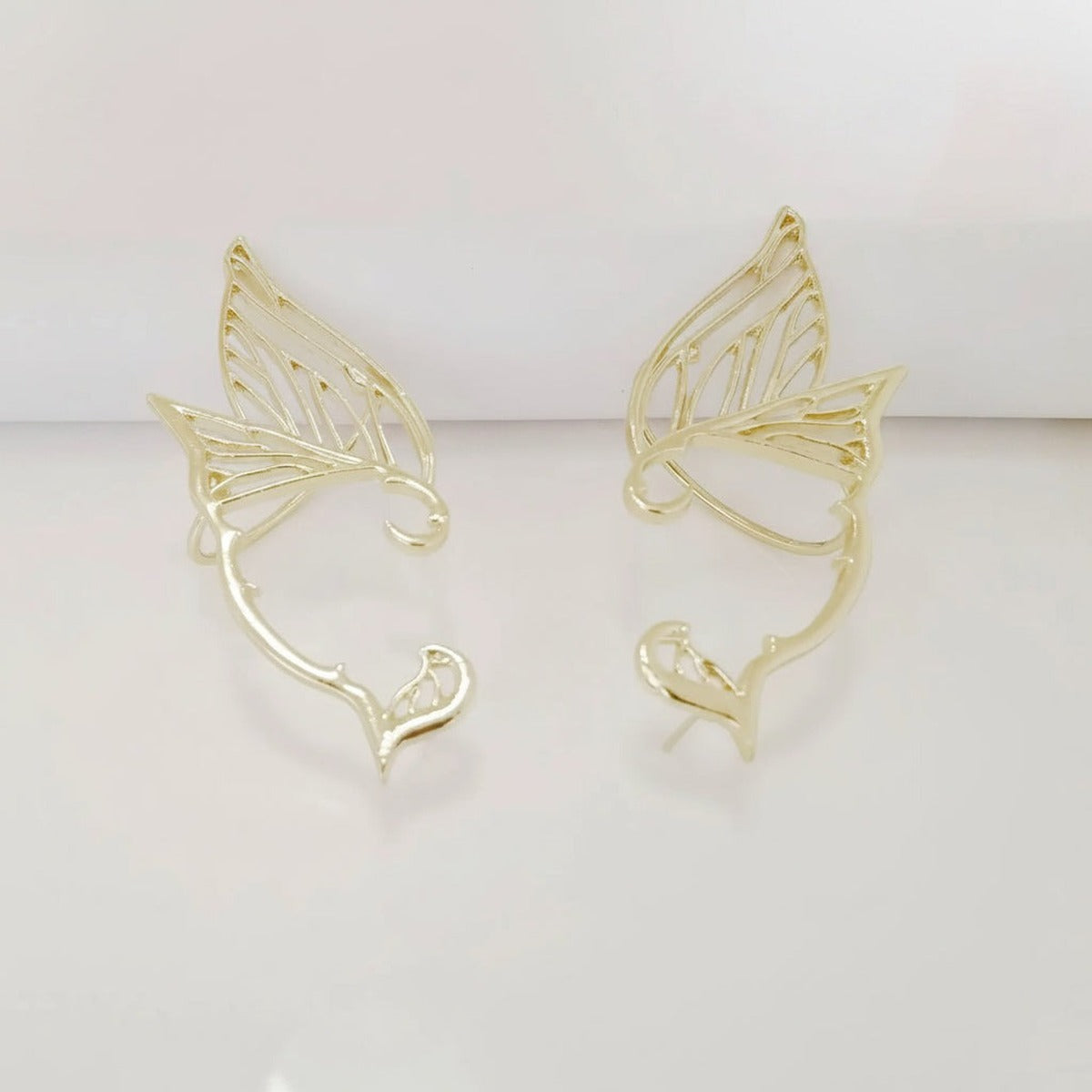 Elven Grace – Elegância Mística – fotografia de estúdio, par de ear cuffs dourados em forma de asa filigranada