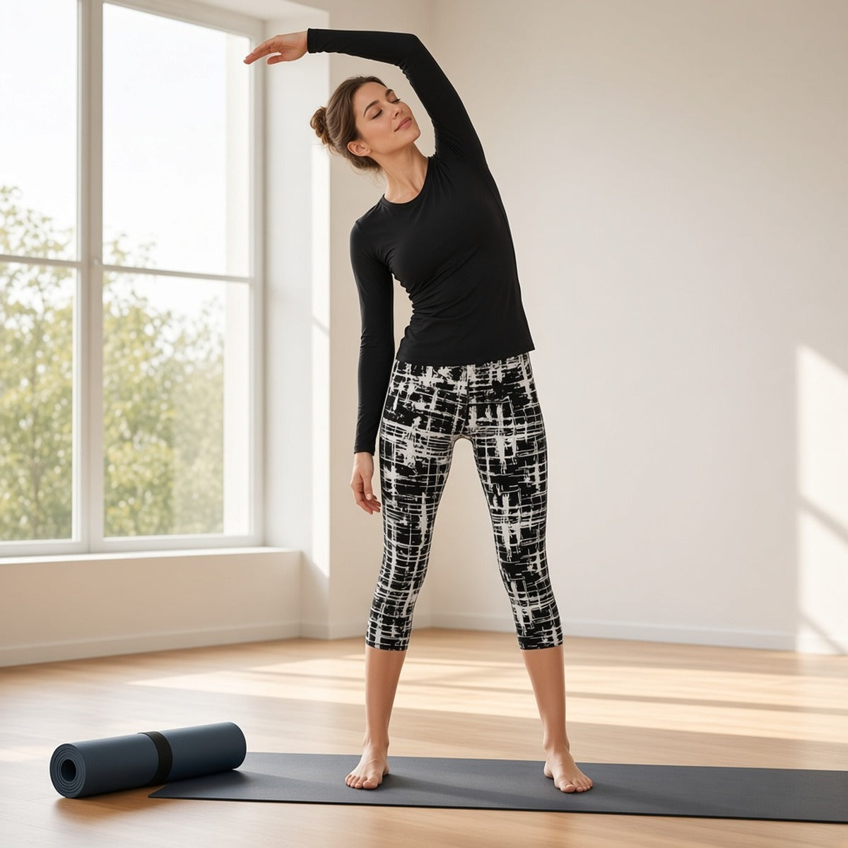 Leggings capri Prisma Flow com padrão preto e branco em alongamento lateral de pé numa sala de yoga com janelas grandes