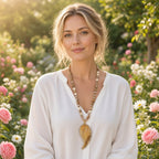 Colar Ayla Wing com contas de pedra bege e pendente de asa em pedra âmbar usado com blusa de linho branca num jardim florido