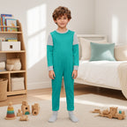 Macacão infantil Abhaya verde-água com mangas cinzentas num menino de pé num quarto luminoso com brinquedos de madeira