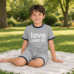 Macacão infantil Maitri cinzento com estampa «love sees all» num menino sentado numa manta num jardim
