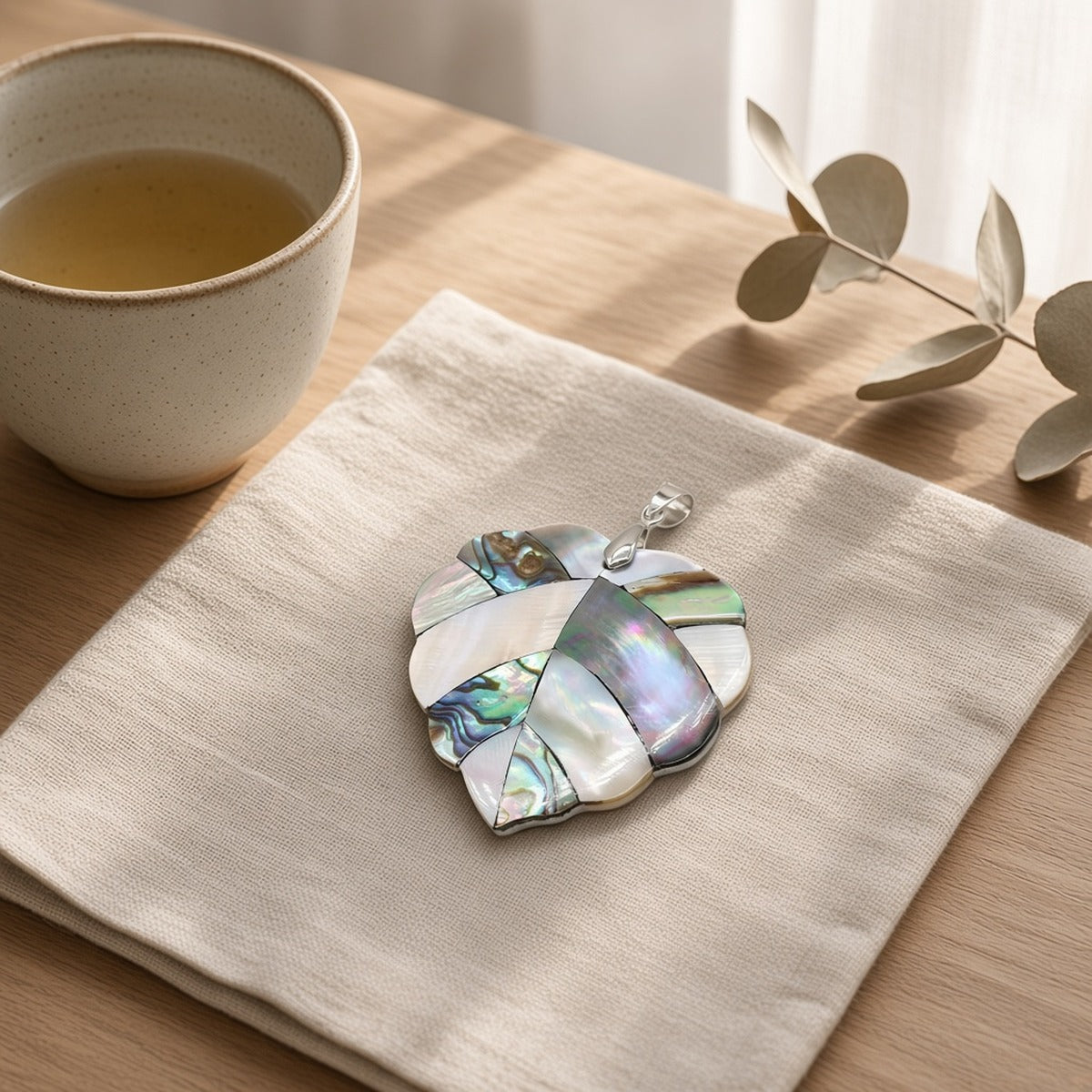 Mother Pearl Flow – Serenidade Natural – lifestyle numa mesa com chá, pendente de madrepérola sobre um guardanapo de linho