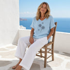 Aura Breeze Blouse – Leveza e Feminilidade – lifestyle numa varanda com vista para o mar, blusa azul-clara com estampa de dentes-de-leão