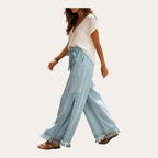 Nahar Bloom – Calças Fluidas de Perna Larga com Racha e Franjas, cor Azul-Claro, vista de lado a caminhar com a racha lateral, fundo estúdio